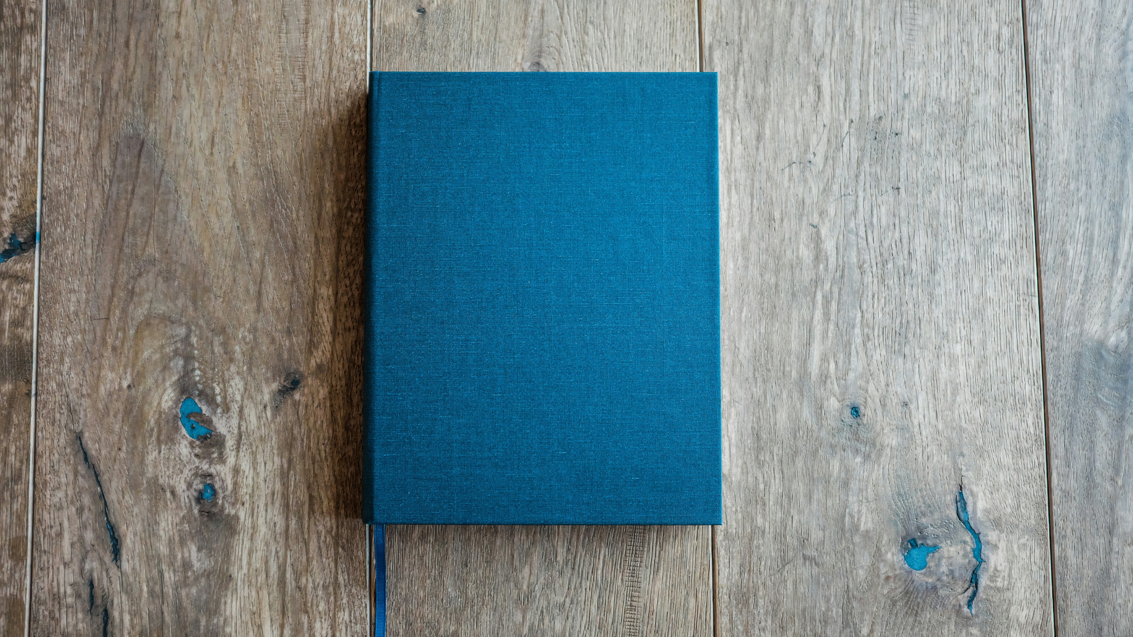 A teal colored hardcover book rests on a distressed wooden tabletop.